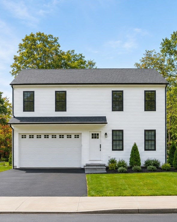 Straight-on front elevation of a newly built white colonial home with a two-car garage, black-trimmed windows and a landscaped front lawn